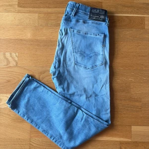 Replay Anbass  - Säljer ett par Replay Anbass jeans i ljusblå tvätt med klassisk femficksdesign och snygga detaljer på bakfickan. Jeansen har en slim passform och är tillverkade i mjukt jeansmaterial med stretch för extra komfort. Perfekt för dig som gillar stilrena och moderna jeans.