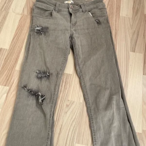 Grå slitna jeans från Gina Tricot - Grå jeans från Gina Tricot med coola slitningar och hål på benen och bakfickan💞💞Klassisk femficksmodell med raka ben och knappgylf. Jättefina och passar till allt!🤗