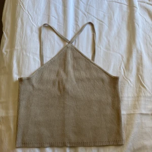 Beige ribbad linnetopp med smala band - Snygg beige ribbad linnetopp med smala axelband som korsas i ryggen. Toppen har en croppad passform och är tillverkad i ett mjukt stickat material som känns skönt mot huden. Perfekt för varma dagar och enkel att matcha med jeans eller kjol.