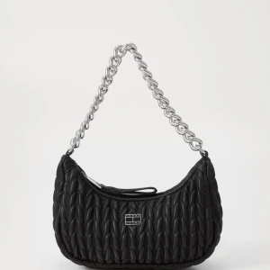 Svart quiltad axelväska från Forét - Snygg svart axelväska från Forét med quiltad yta och grov silverfärgad kedja som axelrem. Väskan har en rundad form och ett metallmärke framtill. Materialet är skinnimitation och stängs med dragkedja upptill. Perfekt för att lyfta din outfit.