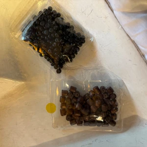 Två sorters pärlor för smyckestillverkning - Säljer två olika sorters pärlor – en påse med svarta runda pärlor och en påse med bruna cylinderformade pärlor. Perfekta för att skapa egna armband, halsband eller andra accessoarer.