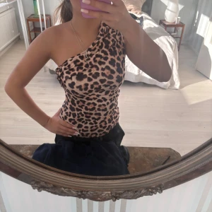 Leopardmönstrad oneshoulder topp - Snygg och trendig oneshoulder topp med leopardmönster. Toppens passform är tight och materialet känns mjukt mot huden. Perfekt för dig som vill sticka ut med ett djurmönster.