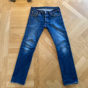 Levis 501 blå jeansbyxor - Klassiska blå Levis 501 jeans med raka ben och fem fickor. Byxorna har knappgylf och tydliga slitningar på framsidan för en snygg vintage-look. Ikonisk Levis-lapp bak i midjan och röd Levis-tagg på bakfickan. Sista två bilderna är hur de sitter på mig som är 190 cm 