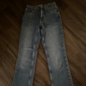 Blå raka jeansbyxor med läderpatch - Klassiska blå jeansbyxor med raka ben och femficksmodell. Byxorna har normal passform och hög midja, samt en brun läderpatch bak i midjan. Perfekta till vardags och enkla att styla med olika toppar. Innerbens längden  är 77 cm, längden på byxorna är 103 cm och midjan är 32 cm. Byxorna är endast provade så de är nya. 🤍🌸 