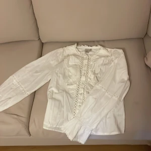 Vit blus med spetsdetaljer från YAS - Säljer en söt vit blus från YAS i storlek S. Blusen har långa ärmar, dekorativa spetsdetaljer och knappar framtill. Perfekt för dig som gillar romantisk och feminin stil. Fräsch och stilren design som passar till mycket.