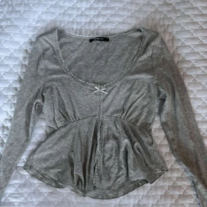 Grå långärmad tröja med spets från Gina Tricot - Supersöt grå långärmad topp från Gina Tricot med spetsdetaljer längs ringningen och en liten rosett framtill. Modellen har en markerad midja och lätt utsvängd nederdel. Aldrig använd därför är den i ny skick. Skriv för frågor eller intresse. 😻