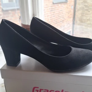 Svarta pumps från Graceland - Säljer ett par klassiska svarta pumps från Graceland med rund tå och klack. Skorna är i syntetmaterial och har en stilren design som passar till många olika outfits. Perfekta för dig som gillar enkel och tidlös stil. Använda enbart två gånger, ena klacken har en liten reva på insidan, men inget som syns när dem är på!