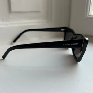 Svarta solglasögon från Saint Laurent Mica YSL276 - Solglasögon från Saint Laurent, svarta i modellen Mica YSL276. Rektangulär form med breda skalmar och diskret logga på sidan. Knappt använda så inte slitna med repor eller liknande. Nypris ca 2700.