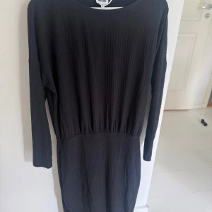 Svart ribbad långärmad klänning - Svart långärmad klänning med ribbad struktur och rund halsringning. Klänningen har en enkel och stilren design som passar perfekt till många olika tillfällen. Tight nertill och lite lösare upp . Endast provad storlek 38 