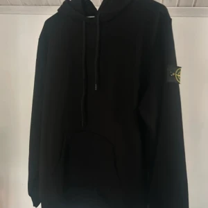 Svart hoodie från Stone Island. S - Säljer en svart hoodie från Stone Island i storlek L. Klassisk modell med huva, dragsko och magficka. Ikonisk Stone Island-logga på vänster ärm. Perfekt för dig som gillar streetwear och stilren design.