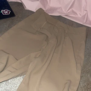 Beiga kostymbyxor med hög midja - Snygga beiga kostymbyxor med hög midja och klassisk stil. stängs med dragkedja och hake. Perfekta för en stilren look.