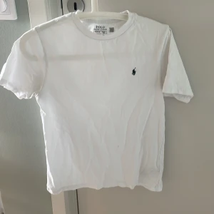 Vit t-shirt från Polo Ralph Lauren - Klassisk vit t-shirt från Polo Ralph Lauren med liten mörkblå broderad logga på bröstet. T-shirten har rund halsringning och är tillverkad i mjuk bomull. Perfekt basic-plagg med normal passform och korta ärmar.