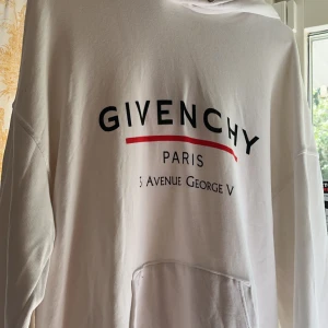 Vit hoodie från Givenchy - Säljer en vit hoodie från Givenchy med tryck på bröstet där det står 'Givenchy Paris 3 Avenue George V' och en röd linje. Hoodien har känguruficka och luva. Perfekt för dig som gillar streetwear och exklusiva märken.