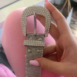 Glittrigt silverbälte med strass - Säljer ett riktigt snyggt bälte i silver med massor av glittrande strass. Bältet har ett brett band och ett stort, rektangulärt spänne som också är täckt av strass. Perfekt för att lyfta vilken outfit som helst.