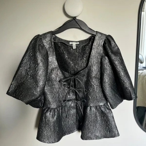 Silvrig blus med puffärmar och snören - Intressekoll på denna glittriga silvriga/svarta blusen från H&M! Kan även användas med ”baksidan framåt” som på sista bilden. Hör av dig vid intresse eller funderingar 🤍