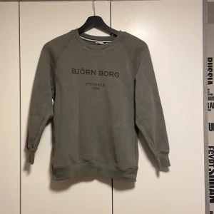 Mörkgrön sweatshirt från Björn Borg - En stilren grå sweatshirt från Björn Borg med tryckt logga och text på bröstet. Tröjan har rund halsringning och långa ärmar. Perfekt för en avslappnad look.