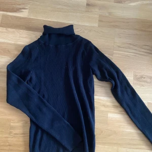 Svart ribbad polotröja - Säljer en svart ribbad polotröja från Lager157 i storlek XS. Tröjan har lång ärm och hög polokrage, perfekt för lager-på-lager och en stilren look. Passar till både jeans och kjol.