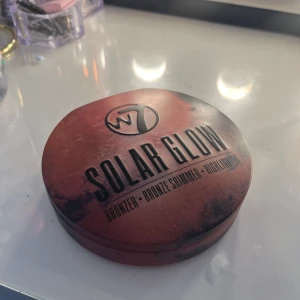 W7 Solar Glow Bronzer, Blush & Highlighter Kit - W7 Solar Glow är en sminkpalett med tre skimrande nyanser: bronzer, contour och highlighter. Kommer i en rund, rödbrun ask och liten borste. Perfekt för att skapa en solkysst look med lyster.