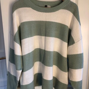 Randig stickad tröja - Säljer en stickad tröja från H&M Divided i grönt och vitt. Tröjan har breda horisontella ränder, rund halsringning och långa ärmar. Den är i storlek L men skulle säga att den är mer som en M 💚🤍