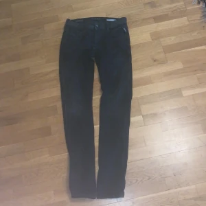 Svarta Replay Hyperflex Anbass jeans - Säljer ett par svarta Replay Hyperflex Anbass jeans med klassisk femficksdesign och raka ben. Jeansen har normal passform och är tillverkade i stretchigt material för extra komfort. Perfekta för dig som vill ha stilrena och bekväma jeans.