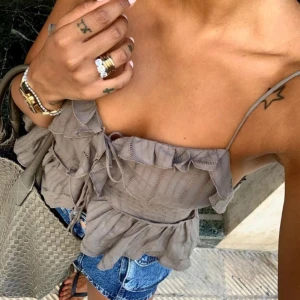 Brun volangtopp med tunna axelband från Zara - Supersöt brun topp med volanger och tunna axelband från Zara. Toppen har knytning framtill och volangdetaljer längs bysten och nederdelen. Perfekt att styla med jeans eller kjol för en trendig look. Säljer även denna i rosa💕