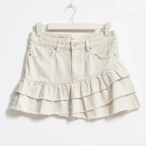 Beige volangkjol i jeans - Säljer en beige kort jeanskjol med volanger och råa kanter. Kjolen har klassiska jeansdetaljer som fickor. Kjolen är helt slutsåld o i super skick!