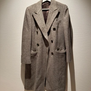 Beige och brun rutig kappa från Sartoria Partenopea - Säljer en klassisk kappa i beige och brunt fiskbensmönster från Sartoria Partenopea. Kappan är tillverkad i 100% ull, har långa ärmar, breda slag och dubbla rader med knappar framtill. Riktig vintage med tyngd. Perfekt för dig som gillar tidlös stil. Foder i silke (sömmar släppt men lätt att justera) innerfickor i mocka. 