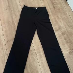 Svarta kostymbyxor från Lindex - Stilrena svarta kostymbyxor från Lindex med raka, vida ben och klassisk passform. Byxorna har knäppning framtill och är perfekta för en dressad look. Passar till många olika tillfällen.