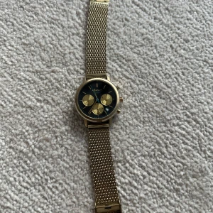 Guldarmbandsklocka från GANT - Stilren klocka från GANT med guldigt mesharmband och svart urtavla. Klockan har tre mindre urtavlor i guld och tydliga markeringar. Perfekt accessoar för att lyfta din outfit.