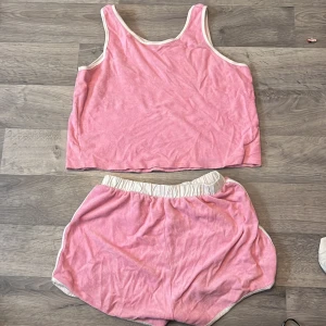Rosa linnetopp och shorts från Primark - Säljer en söt rosa linnetopp med rosa shorts från Primark med vita kanter. Toppen är ärmlös och har en avslappnad passform, perfekt för varma dagar. Materialet är mjukt och bekvämt. 