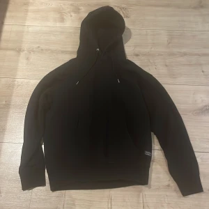 Svart hoodie från Jack & Jones - Säljer en klassisk svart hoodie från Jack & Jones. Tröjan har huva med dragsko och en stor ficka framtill. Perfekt för en avslappnad stil och enkel att matcha med det mesta.