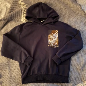 Mörkblå hoodie med Mont-Blanc tryck - Säljer en mörkblå hoodie med Mont-Blanc tryck på bröstet. Tröjan har huva och ribbade muddar vid ärmslut och nederkant. Perfekt för dig som gillar stilrena och bekväma plagg.