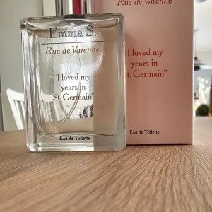 Emma S. Rue de Varenn Eau de Toilette - Endast testad. En elegant parfym med namnet Rue de Varenn från Emma S. Flaskan är genomskinlig med silverfärgad spraydel och text i guld och svart. Doften kommer i en stilren glasflaska på 50 ml och levereras i en ljusrosa kartong.