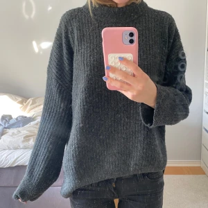 Mörkgrå stickad polotröja - Mysig mörkgrå stickad polotröja med ribbad struktur. Tröjan har lång ärm och en hög polokrage som ger en avslappnad och trendig look. Perfekt för kyligare dagar. Passar nästan alla storlekar!