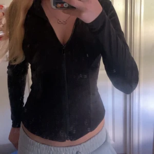 Svart tight zip upp tröja med dragkedja - Säljer en svart, zip upp tröja med hel dragkedja framtill. Den har lång ärm och är tillverkad i ett stretchigt, syntetmaterial som sitter slimmat mot kroppen. Perfekt för dig som gillar en sportig och stilren look.