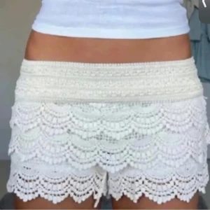Vita virkade spets-shorts - Superfina vita shorts med virkade spetsdetaljer och vågiga kanter. De är högmidjade och har en romantisk, boho-inspirerad look som passar perfekt till sommaren. Materialet känns lätt och luftigt, och shortsen har en snygg volang-effekt.
