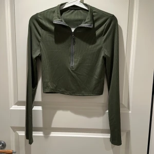 Olivgrön croppad tröja med half zip - Snygg olivgrön croppad tröja med ribbad struktur och half zip-dragkedja framtill. Långärmad modell med hög krage, perfekt om man vill se ut som Kim Possible 