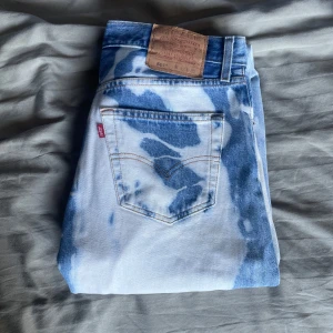 Levis 501 blekta jeans i blått och vitt - Unika Levis 501 jeans med blekt blåvitt mönster. Klassisk rak passform. Jeansen är i kraftig denim och har fem fickor, knappgylf och Levis-lapp bak. Perfekta för dig som vill sticka ut med en cool vintage vibe. Köpta av en konstnär i Newcastle.