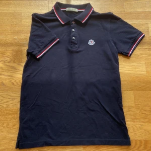 Mörkblå Moncler pikétröja S - Snygg mörkblå pikétröja från Moncler med klassisk krage och knappar framtill. Storlek S