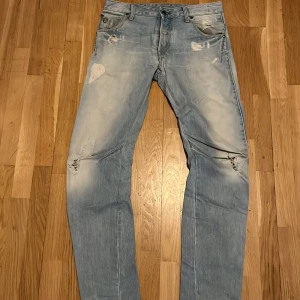 G-Star Raw Arc 3D slim ljusblå slitna jeans - Säljer ett par ljusblå jeans från G-Star med slitna detaljer och snyggt tvättad look. Jeansen har klassisk femficksmodell, dragkedja och raka ben. Perfekta för dig som gillar en avslappnad och trendig stil.