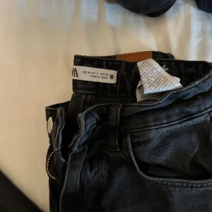 Svarta jeans med råa benslut från Zara - Svarta jeans från Zara i klassisk femficksmodell. Jeansen har hög midja och raka croppade ben med utsvängning, trendiga råa, fransiga benslut. Tillverkade i denim med en mörk tvätt som ger en cool vibe. Perfekta till sneakers eller boots.