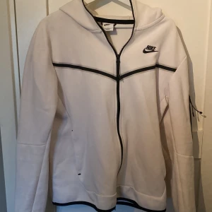 Vit Nike hoodiejacka med svarta detaljer - Nike hoodiejacka i vitt med svarta detaljer och dragkedja framtill. Ny pris 1200kr säljer den för 400kr! Knappt använt passar inte min smak!