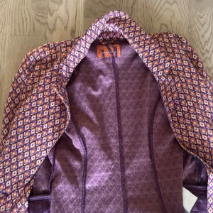 Mönstrad kavaj från Amisu i lila/orange - Säljer en färgstark kavaj från Amisu i storlek 38. Jackan har ett unikt rutigt mönster i lila, orange och vitt, med snygg krage och figursydd passform. Perfekt för dig som vill sticka ut med coola retrovibbar och lekfull stil.