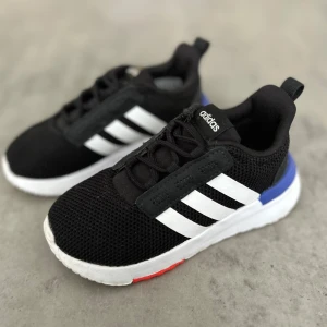 Svarta Adidas sneakers med vita ränder - Snygga svarta Adidas sneakers med klassiska vita ränder på sidorna och vit sula. Skorna har mesh-ovandel för extra andningsförmåga, blå detalj vid hälen och röd detalj under sulan. Perfekta för dig som gillar sportig och stilren look.