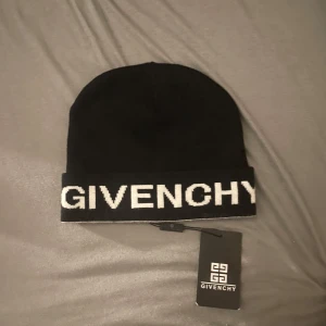 Svart mössa från Givenchy - Helt ny Svart mössa från Givenchy med vit logotyp broderad framtill. Klassisk uppvikt modell i mjukt material med vit insida. Perfekt accessoar för att lyfta din streetwear-look och hålla dig varm under kyliga dagar.