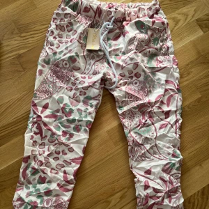 Mönstrade byxor från Chica London - Snygga byxor från Chica London med blommigt och leopardinspirerat mönster i rosa, grönt och beige. Byxorna har dragsko i midjan och är tillverkade i mjuk polyester med lite stretch. Perfekta för dig som vill sticka ut med färg och mönster. One size 