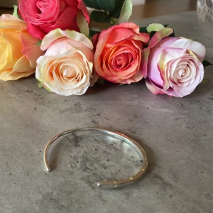 Silverfärgat armband  - Stilrent och minimalistiskt armband från Pandora i silverfärg (inte riktig). Armbandet är stelt och öppet, med diskret graverad text 'PANDORA' längs ovansidan. Perfekt för dig som gillar enkel och klassisk design.