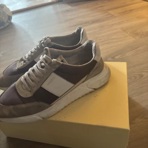 Bruna sneakers från Axel Arigato - Snygga sneakers från Axel Arigato i brunt och beige med vita detaljer. Skorna har en chunky vit sula, snörning och paneler i mocka och textil. Perfekta för dig som gillar stilrena och trendiga sneakers med en sportig vibe.
