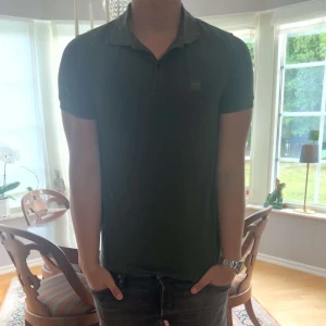 Hugo boss piké  - Snygg grön pikétröja från BOSS med klassisk krage och korta ärmar. Tröjan har diskret logga på bröstet och är tillverkad i bomull för en skön känsla. Perfekt till jeans eller shorts för en clean look.