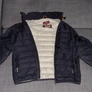 Svart dunjacka från Parajumpers Y-M - Säljer en svart dunjacka från Parajumpers i modellen Super Lightweight. Jackan har quiltad design, lång ärm, dragkedjor på fickorna och coolt PJS-märke på ärmen. Insidan är ljus och jackan är perfekt för dig som vill ha en lätt och snygg jacka med streetkänsla.